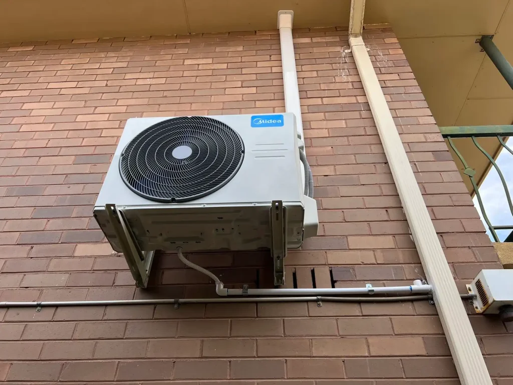 Midea air conditioning unit installed on a brick wall outside a building with pipes and wiring